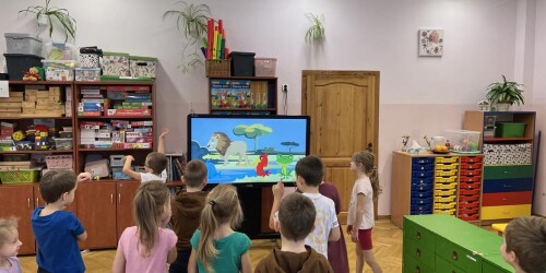 dzieci wykonują ćwiczenia gimnastyczne prezentowane przez zwierzątka na tablicy interaktywnej